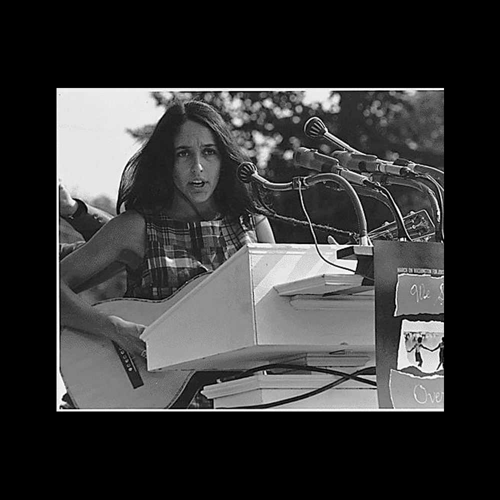 Joan Baez holding a guitar at a podium during the 1963 Civil Rights March on Washington D.C.